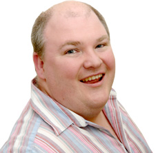 Spencer is smiling. He has short light hair, wearing a striped shirt in soft pastel colors. He is posing against a plain white background.